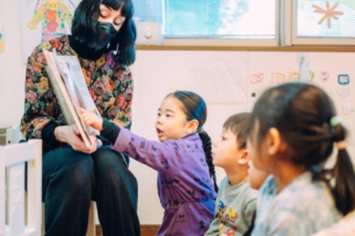 先生の読み聞かせに手を伸ばして答える子どもたち