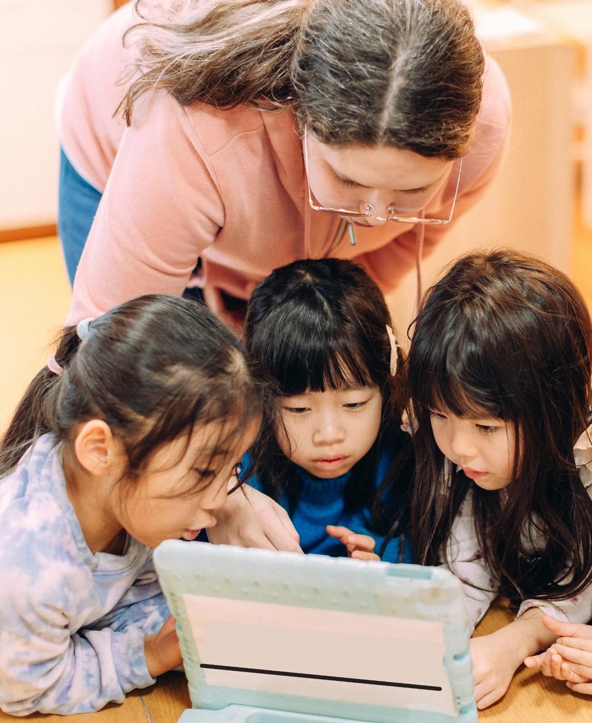 タブレットを囲み、先生と顔を寄せ合って対話する子どもたち